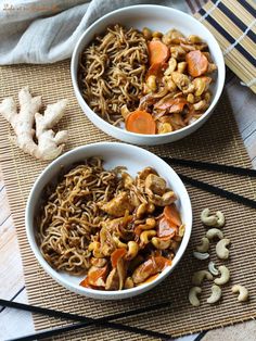 two bowls filled with noodles, carrots and cashews next to chopsticks