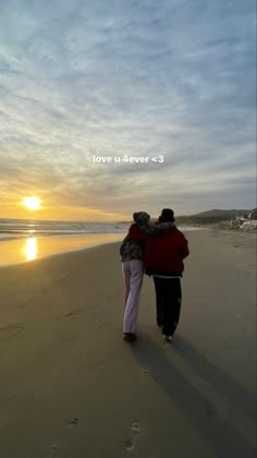 two people are walking on the beach with their arms around each other as the sun sets