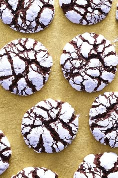 several chocolate crinkle cookies are on a yellow surface with white powdered sugar