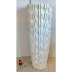 a tall white vase sitting on top of a tile floor next to a can of soda