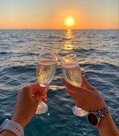 two people toasting with wine glasses in front of the ocean at sunset or sunrise