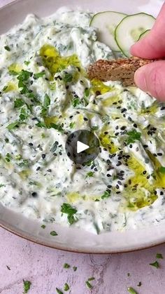 a person dipping some kind of food into a bowl with cucumber and olives