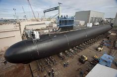 a large black submarine sitting on top of a building next to other boats and cranes