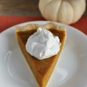 a slice of pumpkin pie with whipped cream on top sits on a plate next to a small pumpkin