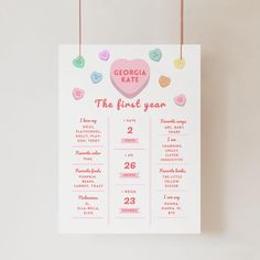 a pink and blue heart themed first year calendar hangs on a white wall with hearts