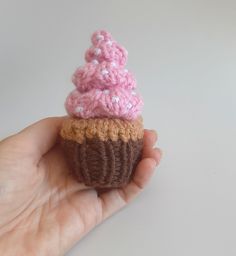 a hand holding a tiny crocheted cupcake with pink frosting and sprinkles