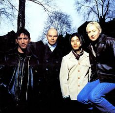 a group of people standing next to each other in front of some trees and buildings