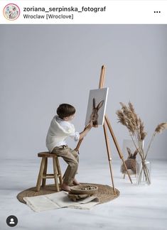 a young boy sitting on a stool in front of an easel