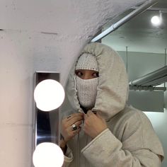 a person in a hoodie is fixing something on the mirror with lights around them