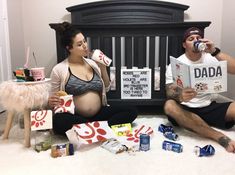 a man and woman sitting on the floor next to a baby crib drinking from cups