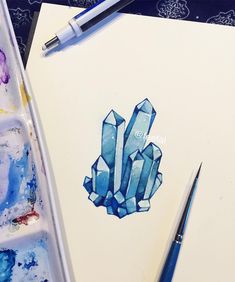 a watercolor drawing of blue crystals on paper next to a paintbrush and brush