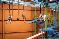 a woman and two children are on the ropes in an indoor climbing area, while another child watches