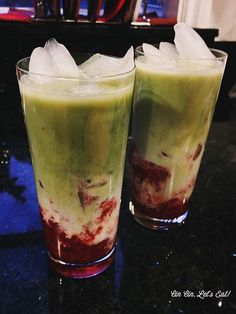 two glasses filled with green and red liquid on top of a table next to each other