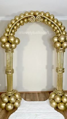 an arch made out of gold balls on top of a white sheeted bed in front of a wall