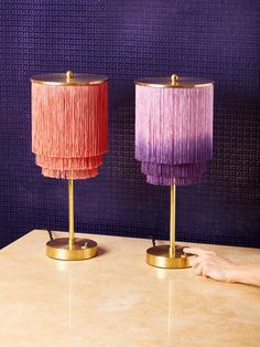 two lamps with fringe shades on them sitting on a table next to a purple wall