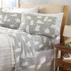 a bed covered in white and grey sheets with polar bears on them, sitting next to a night stand