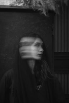 a woman with long hair wearing a black hoodie is standing in front of a wall