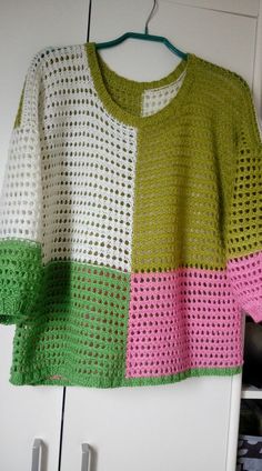 a crocheted sweater hanging on a clothes hanger in front of a white cabinet