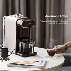 a coffee maker sitting on top of a white table next to a cup of coffee