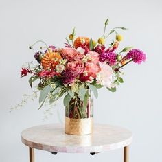 a vase filled with lots of flowers on top of a marble table next to a white wall