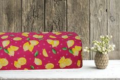 a pink bag with yellow lemons on it next to a small vase filled with flowers