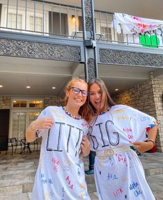 two women in white dresses standing next to each other holding up t - shirts with writing on them