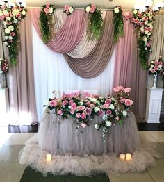 a table with flowers and candles on it in front of a curtained wall that is decorated with tulle