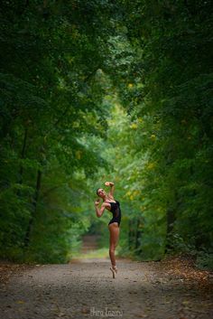 a woman running down a dirt road in the middle of a forest with lots of trees