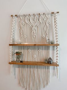 a macrame wall hanging with two wooden shelves