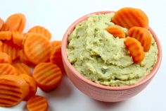 a pink bowl filled with carrots and guacamole next to some cut up pieces