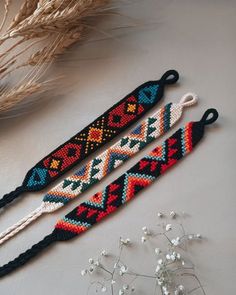 three beaded bracelets on a table next to some dried grass and flowers in the background