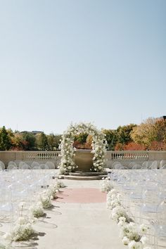 an outdoor ceremony setup with white flowers and greenery on the aisle, surrounded by rows of chairs