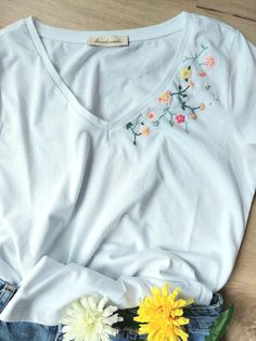 a white t - shirt with flowers on it sitting next to some blue jean shorts