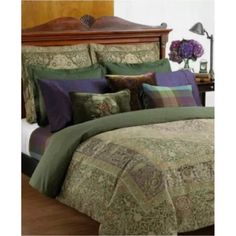 a bed with green and purple comforters on top of it next to a wooden headboard