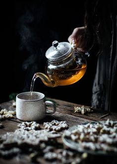 a person pouring tea into a cup on top of a wooden table filled with dried flowers