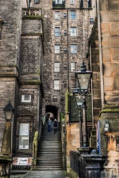 an old stone building with stairs leading up to the top floor and two people walking down it