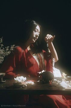 a woman sitting at a table with a teapot in her hand and flowers on the table