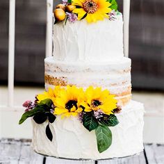 a three tiered cake with sunflowers and leaves on the top is sitting on a wooden table