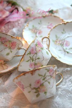 tea cups and saucers with pink flowers on them sitting on a lace tablecloth