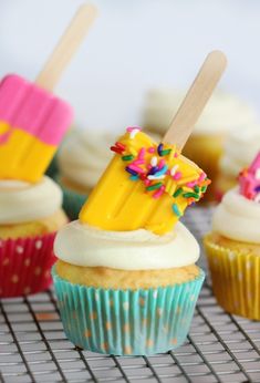 cupcakes with colorful frosting and popsicle toppers on a cooling rack