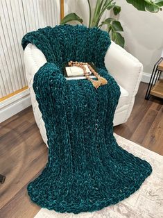 a green knitted blanket sitting on top of a white chair next to a plant