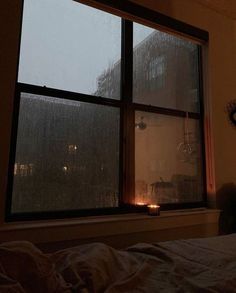 there is a candle that is lit in front of the window with rain coming down