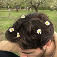 a man with three daisies in his hair sitting on the ground next to trees