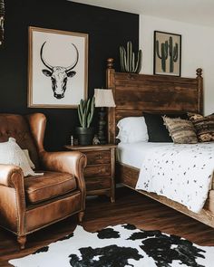 a bedroom with black walls and white bedding, brown leather chair and cow rug