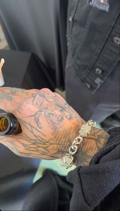 a man with tattoos on his arm holding a beer bottle and chain around his wrist