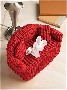 a red knitted heart shaped box sitting on top of a table next to a book