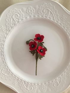 three red flowers are placed in the center of a white plate on a tablecloth