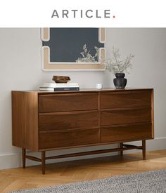 a wooden dresser sitting in front of a mirror and vase on top of the dresser