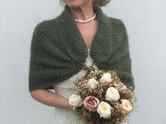 a woman holding a bouquet of flowers wearing a green knitted shawl over her shoulders