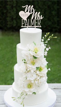 a wedding cake with white flowers and a monogrammed topper is on a wooden table